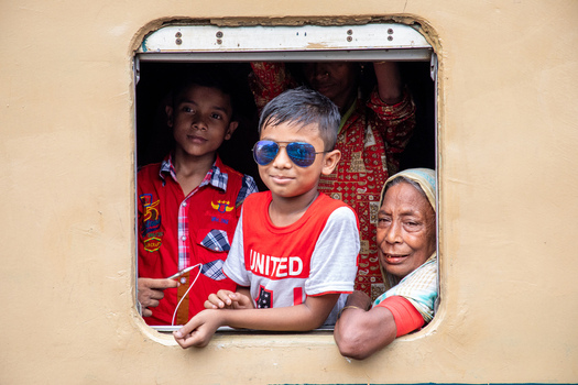 Dhaka Bangladesh 14 June 2018 View of people looking out of a train window at Airport Railway Station including a young boy wearing blue sunglasses and an elderly woman. Dhaka Bangladesh 14 June 2018 View of people looking out of a train window at Airport Railway Station including a young boy wearing blue sunglasses and an elderly woman.