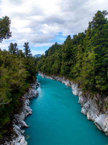 Aerial view of a vibrant turquoise river slicing through a dense emerald forest the rugged banks a stark contrast under a cloudy sky Hokitika Gorge New Zealand. Aerial view of a vibrant turquoise river slicing through a dense emerald forest the rugged banks a stark contrast under a cloudy sky Hokitika Gorge New Zealand.