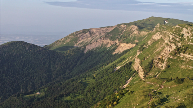Aerial view of Col de la Faucille featuring rugged mountain ridges lush green slopes dense forests and a winding trail in Gex Auvergne Rhone Alpes France.