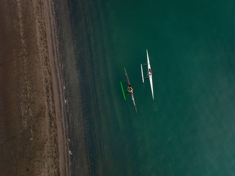 Raglan New Zealand 09 February 2026 Aerial view of two outrigger canoes paddling on the calm turquoise water near the sandy shoreline.