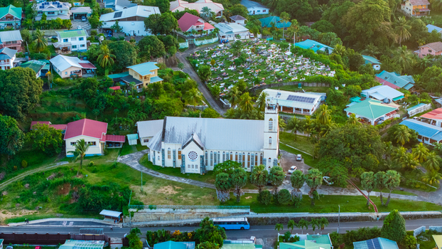 Aerial view of a historic church surrounded by lush tropical greenery residential houses and a nearby cemetery in Mahe Baie Lazare Seychelles.