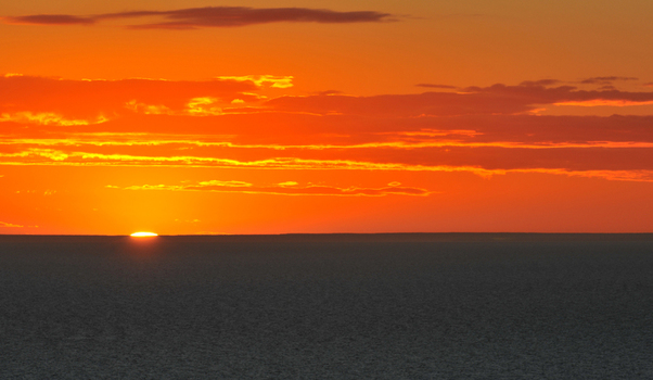 View of the sun setting over the ocean horizon with vibrant orange and red clouds at Puerto Piramides Puerto Madryn Chubut Argentina. View of the sun setting over the ocean horizon with vibrant orange and red clouds at Puerto Piramides Puerto Madryn Chubut Argentina.