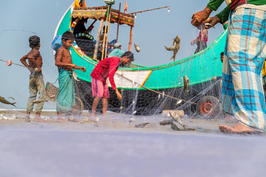 Teknaf Bangladesh 10 March 2026 View of young boys in their colourful clothes helping fishermen with the day s catch by the turquoise boat on the sandy shore.