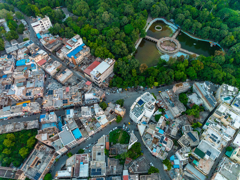 Aerial view of the dense urban landscape of Udaipur featuring residential buildings lush green trees and a pond with a circular structure Udaipur Rajasthan India.