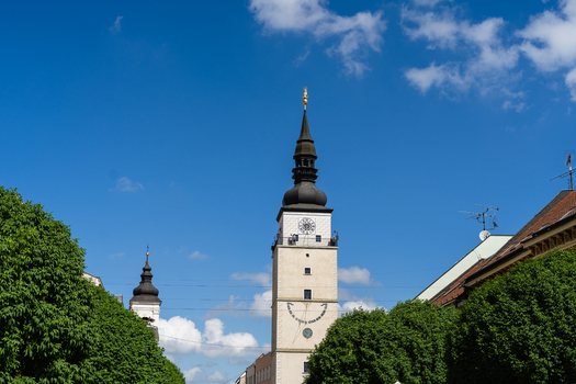View of the historic City Tower with its distinctive dark spire and golden statue framed by lush green trees under a blue sky in Trnava Trnava Region Slovakia. View of the historic City Tower with its distinctive dark spire and golden statue framed by lush green trees under a blue sky in Trnava Trnava Region Slovakia.