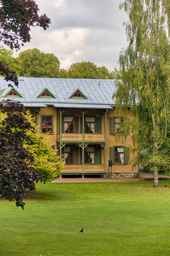 Ronneby Sweden 11 September 2025 View of a historic wooden villa in Brunssparken featuring traditional yellow timber architecture green shutters and a balcony set within a lush park. Ronneby Sweden 11 September 2025 View of a historic wooden villa in Brunssparken featuring traditional yellow timber architecture green shutters and a balcony set within a lush park.