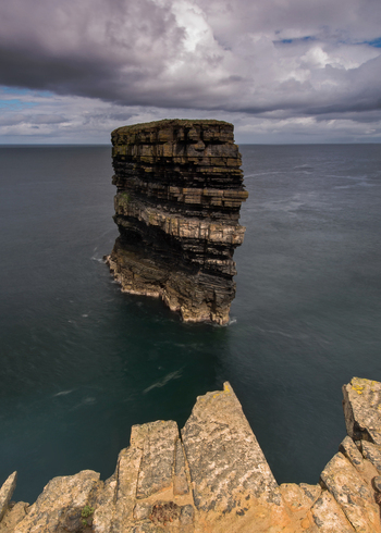 View of Dun Briste Sea Stack rising from the Atlantic Ocean with layered rock formations under a cloudy sky County Mayo Ireland. View of Dun Briste Sea Stack rising from the Atlantic Ocean with layered rock formations under a cloudy sky County Mayo Ireland.
