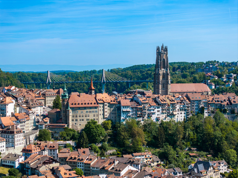 Aerial view of St Nicolas Cathedral and the historic old town with red tiled rooftops the modern Poya Bridge and lush green hills under a clear blue sky in Fribourg Fribourg Switzerland. Aerial view of St Nicolas Cathedral and the historic old town with red tiled rooftops the modern Poya Bridge and lush green hills under a clear blue sky in Fribourg Fribourg Switzerland.