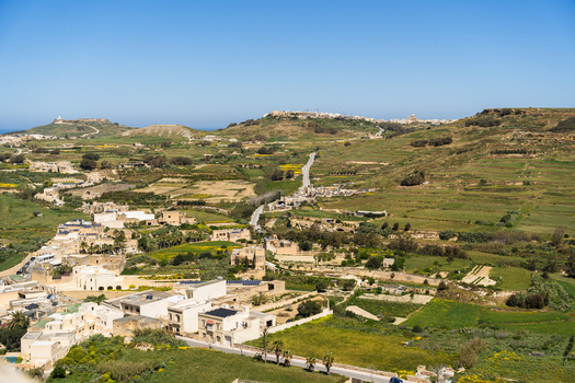 View of traditional limestone houses and terraced agricultural fields across the rolling green hills under a clear blue sky in Zebbug Gozo Region Malta. View of traditional limestone houses and terraced agricultural fields across the rolling green hills under a clear blue sky in Zebbug Gozo Region Malta.