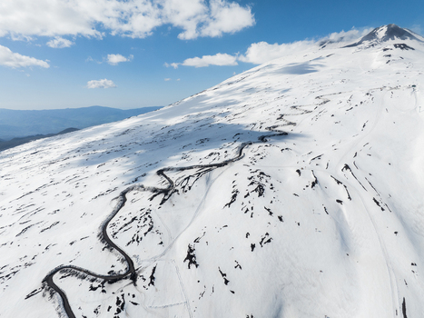 Aerial view of the snow covered south slope of Mount Etna with a winding road snaking through the volcanic landscape under a blue sky in Nicolosi Sicilia Italy. Aerial view of the snow covered south slope of Mount Etna with a winding road snaking through the volcanic landscape under a blue sky in Nicolosi Sicilia Italy.