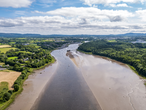 Aerial view of the River Moy flowing through the town of Ballina with lush green fields mudflats and small boats under a cloudy sky in Ballina County Mayo Ireland.