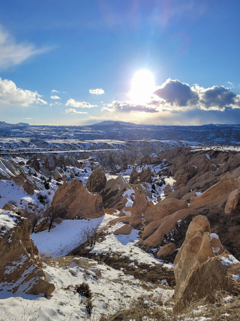 View of the snow covered fairy chimneys and unique rock formations of Cappadocia under a bright winter sun and blue sky in Turkiye. View of the snow covered fairy chimneys and unique rock formations of Cappadocia under a bright winter sun and blue sky in Turkiye.