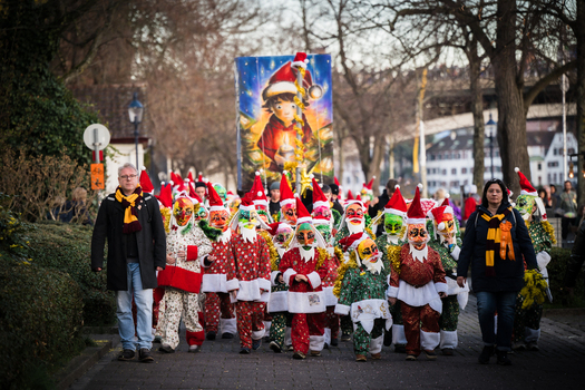 Basel Switzerland 10 March 2025 View of a vibrant procession of masked figures in red and green festive costumes marches down Fasnacht a large banner of a child in a Santa hat held aloft. Basel Switzerland 10 March 2025 View of a vibrant procession of masked figures in red and green festive costumes marches down Fasnacht a large banner of a child in a Santa hat held aloft.