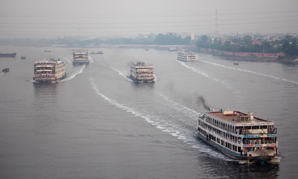 Munshiganj Bangladesh 04 April 2026 Aerial view of multiple ferries cutting through the murky river each leaving a foamy white trail against the dark water. Munshiganj Bangladesh 04 April 2026 Aerial view of multiple ferries cutting through the murky river each leaving a foamy white trail against the dark water.