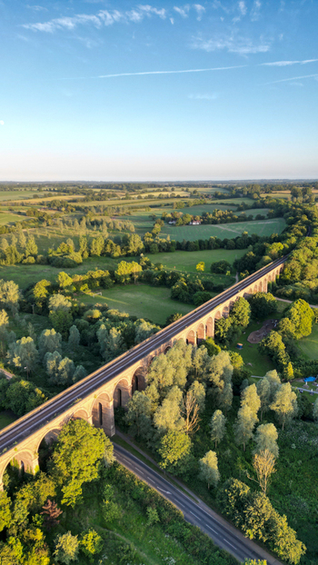 Aerial view of the historic Chappel Viaduct stretching across the lush green countryside with surrounding trees and a road below in Chappel England United Kingdom.