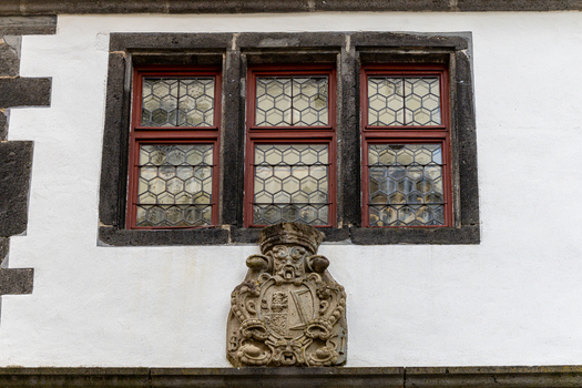 View of the historic facade of Eltz Castle featuring a stone coat of arms and traditional leaded glass windows with red frames Wierschem Rhineland Palatinate Germany.
