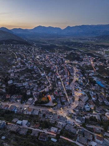 Aerial view of the coastal city of Saranda at twilight with illuminated streets residential buildings and surrounding mountains in Saranda Vlore County Albania. Aerial view of the coastal city of Saranda at twilight with illuminated streets residential buildings and surrounding mountains in Saranda Vlore County Albania.