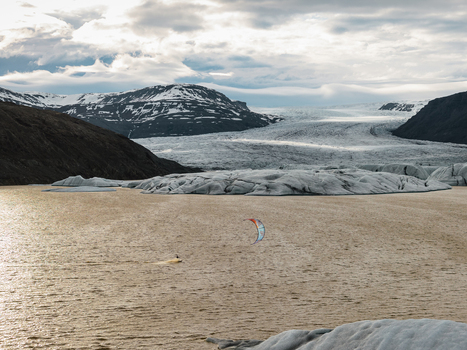 Aerial view of a kiteboarder gliding across the glacial waters of Vatnajokull with the massive ice cap and rugged mountains in the background Iceland.