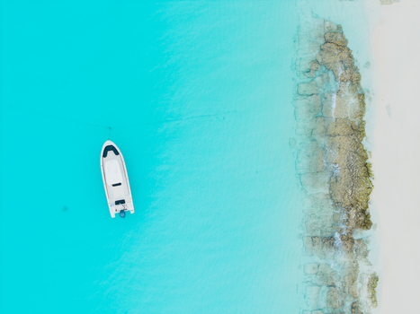 Aerial view of a lone white boat adrift in the turquoise water near the sandy shores Vashafaru Island Maldives. Aerial view of a lone white boat adrift in the turquoise water near the sandy shores Vashafaru Island Maldives.