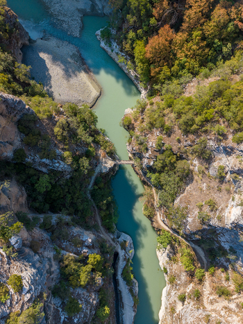 Aerial view of Osumi canyon featuring a winding river flowing through steep rocky cliffs and lush forest with a small bridge crossing the water in Dhores Berat County Albania.