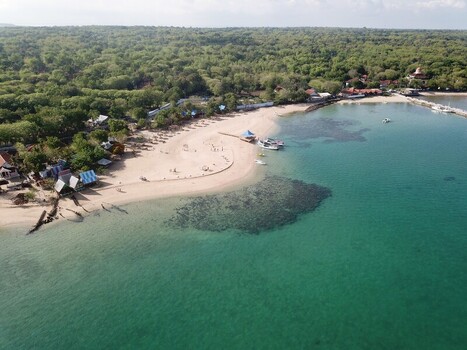 Aerial view of a sandy beach with turquoise water coral reefs small boats and lush greenery along the coastline in Sumenep East Java Indonesia.