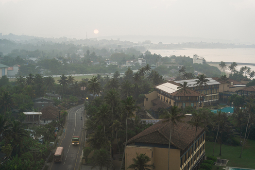 View of the coastal town landscape with palm trees a winding road and buildings under a hazy sunset sky in Galle Southern Province Sri Lanka.