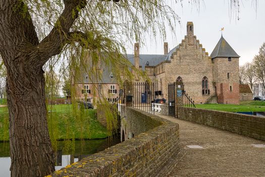View of Radboud Castle with its historic brick walls and a stone bridge over the moat framed by a weeping willow tree in Medemblik Noord Holland Netherlands. View of Radboud Castle with its historic brick walls and a stone bridge over the moat framed by a weeping willow tree in Medemblik Noord Holland Netherlands.