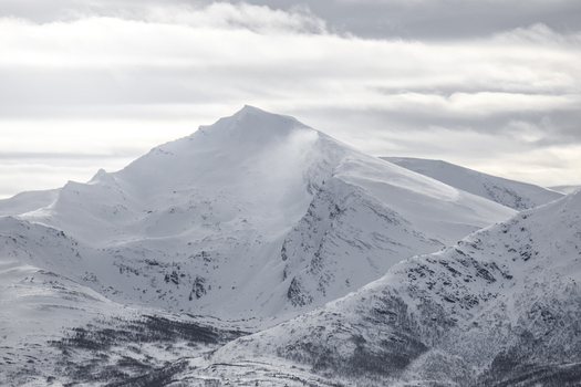 View of snow covered mountain peaks under a cloudy winter sky with sparse vegetation in the foreground Tromso Troms Norway.