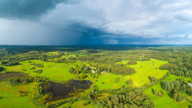 Aerial view of lush green fields dense forests and small ponds under a dramatic stormy sky in Latvia. Aerial view of lush green fields dense forests and small ponds under a dramatic stormy sky in Latvia.