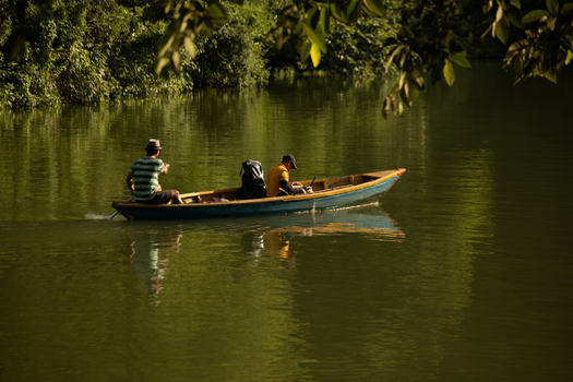 Pokhara Nepal 31 July 2026 View of two men rowing a small wooden boat across the calm river surrounded by lush green trees in the afternoon light.