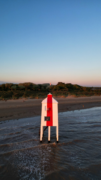 Aerial view of the historic Burnham on Sea Low Lighthouse standing on wooden stilts on the sandy beach at sunset with calm waves and coastal vegetation in Burnham on Sea England United Kingdom. Aerial view of the historic Burnham on Sea Low Lighthouse standing on wooden stilts on the sandy beach at sunset with calm waves and coastal vegetation in Burnham on Sea England United Kingdom.