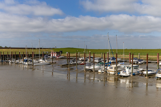 View of boats moored to wooden pilings in the harbor of Dangast at low tide with a green dike under a cloudy sky Varel Lower Saxony Germany.