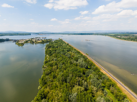 Aerial view of the Danube river featuring a lush green forested island and a long embankment path under a bright blue sky Bratislava Bratislava Region Slovakia. Aerial view of the Danube river featuring a lush green forested island and a long embankment path under a bright blue sky Bratislava Bratislava Region Slovakia.