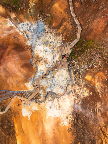 Aerial view of a wooden boardwalk winding through a geothermal landscape with steaming vents and colorful mineral deposits in Iceland. Aerial view of a wooden boardwalk winding through a geothermal landscape with steaming vents and colorful mineral deposits in Iceland.