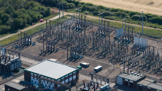Aerial view of the electrical substation with metal structures transformers and power lines surrounded by green fields and trees in Bishops Stortford England United Kingdom. Aerial view of the electrical substation with metal structures transformers and power lines surrounded by green fields and trees in Bishops Stortford England United Kingdom.