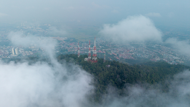 Aerial view of telecommunication towers atop the forested Tokun Hill surrounded by low hanging clouds with the urban landscape of Bukit Mertajam Penang Malaysia. Aerial view of telecommunication towers atop the forested Tokun Hill surrounded by low hanging clouds with the urban landscape of Bukit Mertajam Penang Malaysia.