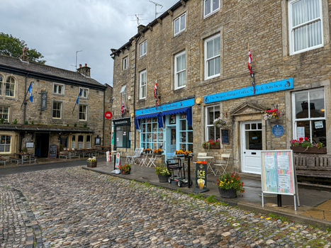Grassington UK 17 May 2026 View of the historic stone buildings and cobblestone street featuring The Stripey Badger bookshop and coffee shop under a cloudy sky. Grassington UK 17 May 2026 View of the historic stone buildings and cobblestone street featuring The Stripey Badger bookshop and coffee shop under a cloudy sky.