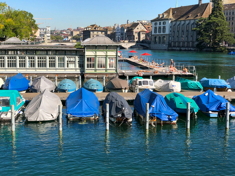 View of boats covered with tarps moored at a floating dock on the Limmat river with people sunbathing on a wooden platform in the background in Zurich Zurich Switzerland.