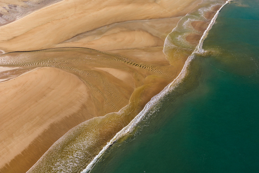 Aerial view of the sandy beach with intricate water patterns and turquoise sea waves breaking on the shore in Plurien Brittany France. Aerial view of the sandy beach with intricate water patterns and turquoise sea waves breaking on the shore in Plurien Brittany France.