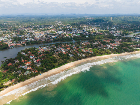 Aerial view of the coastal town with sandy beaches turquoise ocean waves and the Nilwala River flowing through lush greenery Matara Southern Province Sri Lanka. Aerial view of the coastal town with sandy beaches turquoise ocean waves and the Nilwala River flowing through lush greenery Matara Southern Province Sri Lanka.