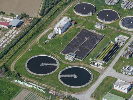Aerial view of a modern water treatment plant featuring circular sedimentation tanks and rectangular basins surrounded by green fields in Paestum Campania Italy.