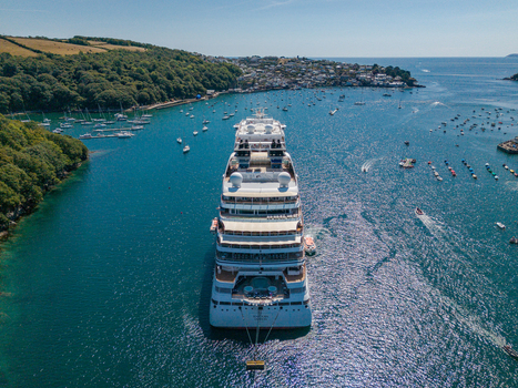 Fowey Cornwall United Kingdom 10 August 2026 Aerial view of a cruise ship anchored in the Fowey River with the town of Fowey small boats and green hills under a clear sky. Fowey Cornwall United Kingdom 10 August 2026 Aerial view of a cruise ship anchored in the Fowey River with the town of Fowey small boats and green hills under a clear sky.
