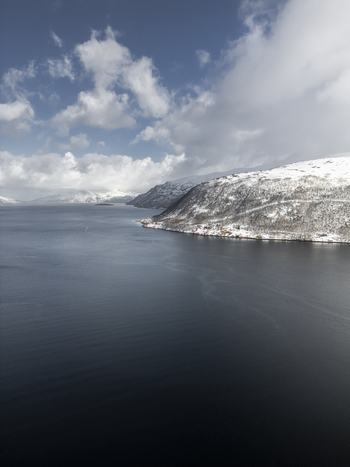 Aerial view of Grotfjord with snow capped mountains and dark blue water under a cloudy sky in Tromvik Troms Norway. Aerial view of Grotfjord with snow capped mountains and dark blue water under a cloudy sky in Tromvik Troms Norway.