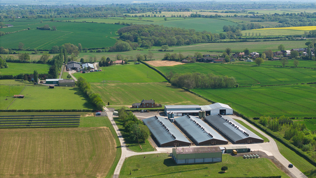 Aerial view of an industrial farm facility with large sheds and solar panels surrounded by lush green fields and meadows in Kettering England United Kingdom. Aerial view of an industrial farm facility with large sheds and solar panels surrounded by lush green fields and meadows in Kettering England United Kingdom.