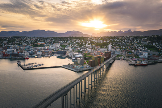 Aerial view of the Tromso Bridge spanning the water with the city of Tromso nestled against mountains under a golden sunset sky in Tromso Troms Norway. Aerial view of the Tromso Bridge spanning the water with the city of Tromso nestled against mountains under a golden sunset sky in Tromso Troms Norway.
