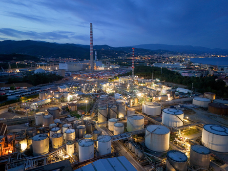 Aerial view of a lubricant production plant featuring numerous storage tanks and industrial chimneys illuminated at dusk with the coastal city in the background Vado Ligure Liguria Italy. Aerial view of a lubricant production plant featuring numerous storage tanks and industrial chimneys illuminated at dusk with the coastal city in the background Vado Ligure Liguria Italy.