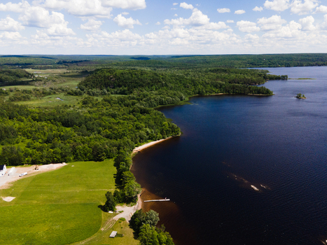 Aerial view of Commanda Lake featuring a lush green forest shoreline a sandy beach and calm dark blue waters under a bright sky in Restoule Ontario Canada. Aerial view of Commanda Lake featuring a lush green forest shoreline a sandy beach and calm dark blue waters under a bright sky in Restoule Ontario Canada.