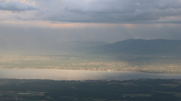 Aerial view of Le Colomby de Gex overlooking the Jura mountains and Lake Geneva under a dramatic cloudy sky with sunbeams in Echenevex Auvergne Rhone Alpes France. Aerial view of Le Colomby de Gex overlooking the Jura mountains and Lake Geneva under a dramatic cloudy sky with sunbeams in Echenevex Auvergne Rhone Alpes France.