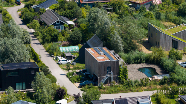 Aerial view of Ecodorp Bolderburen featuring sustainable modern houses with green roofs and solar panels surrounded by lush greenery and a small pond in Almere Flevoland Netherlands. Aerial view of Ecodorp Bolderburen featuring sustainable modern houses with green roofs and solar panels surrounded by lush greenery and a small pond in Almere Flevoland Netherlands.