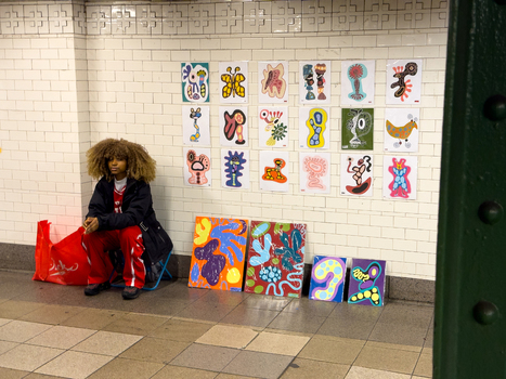 New York United States 14 May 2026 View of a young artist sitting by her colorful abstract illustrations displayed on a white tiled wall in a subway station. New York United States 14 May 2026 View of a young artist sitting by her colorful abstract illustrations displayed on a white tiled wall in a subway station.